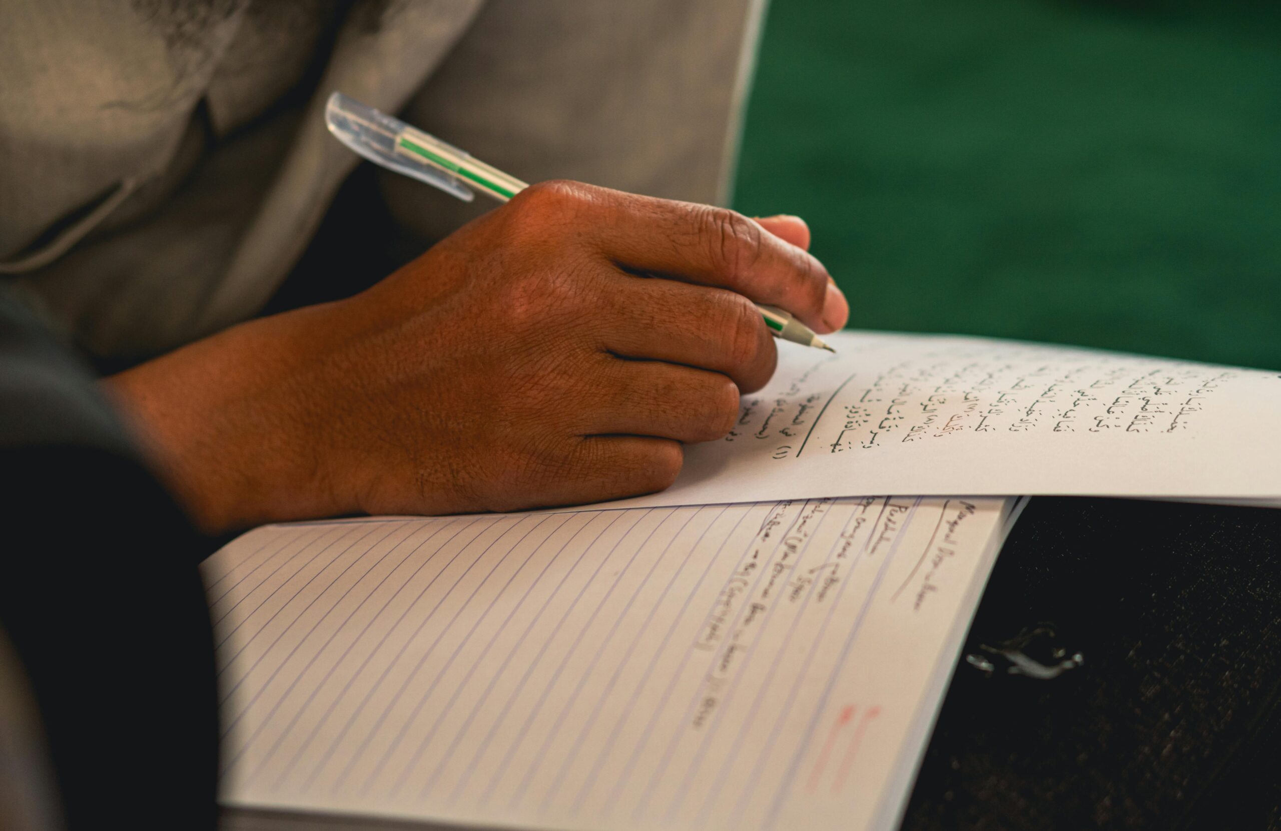 Detailed view of a person's hand writing with a pen on paper in Arabic script.